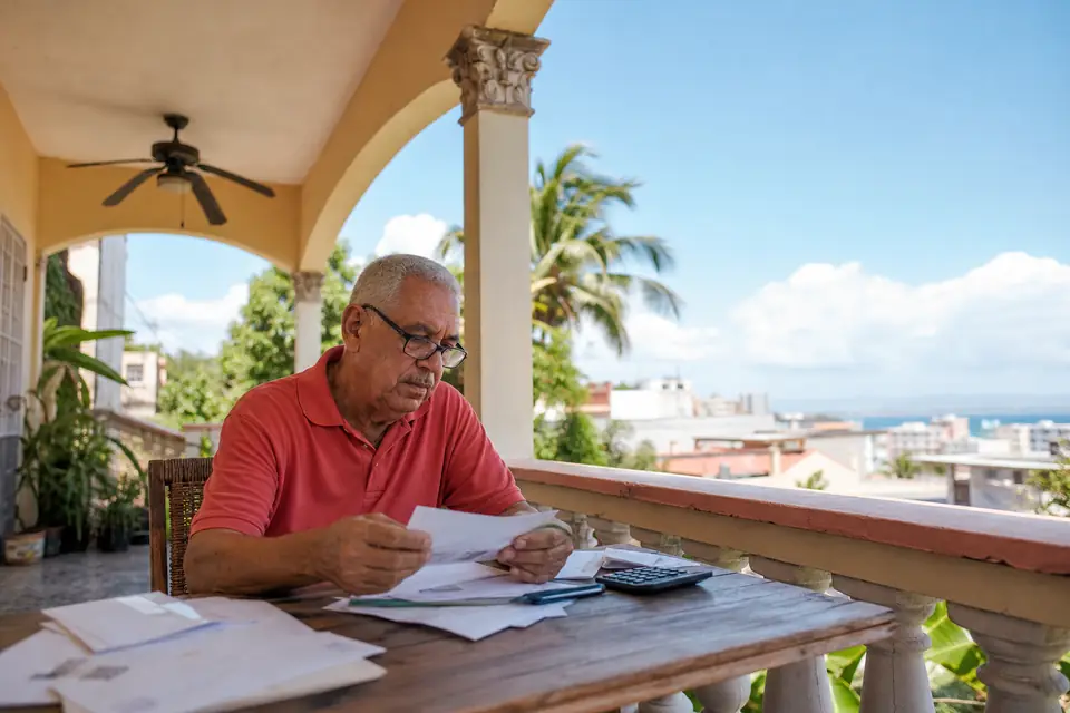 Hombre jubilado organiza sobres y usa una calculadora en el balcón de su casa.