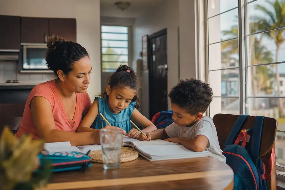 Madre ayuda a sus dos hijos con las tareas en la mesa de la cocina