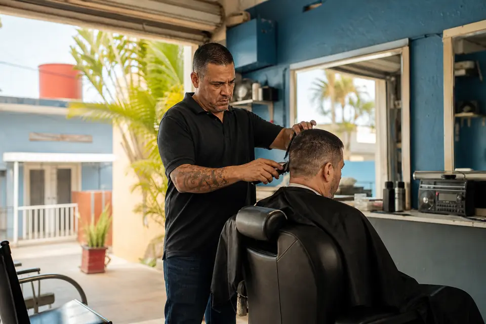 Barbero corta el pelo a un cliente en su barbería de Arecibo