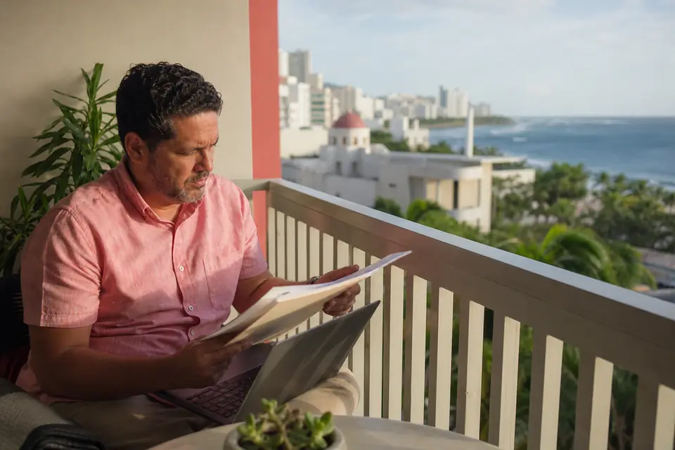 Hombre trabaja con una computadora portátil en un balcón frente al mar en Condado