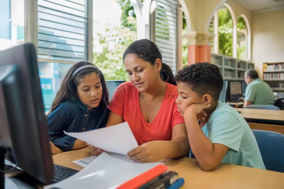 Madre revisa un formulario con sus dos hijos en una biblioteca pública