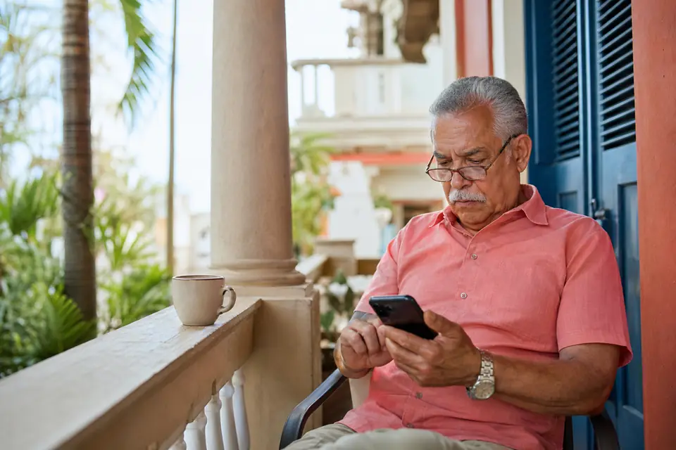 Hombre mayor revisa en su celular el estado de su reintegro en el balcón